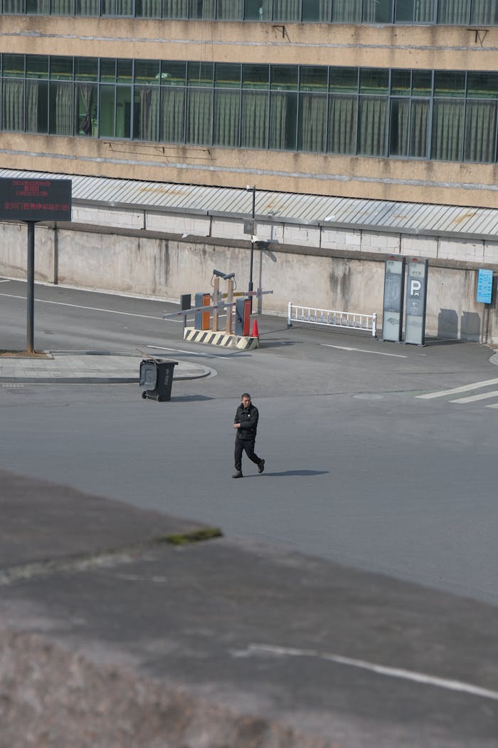 Services A lone security guard patrols an empty urban parking area during the day.