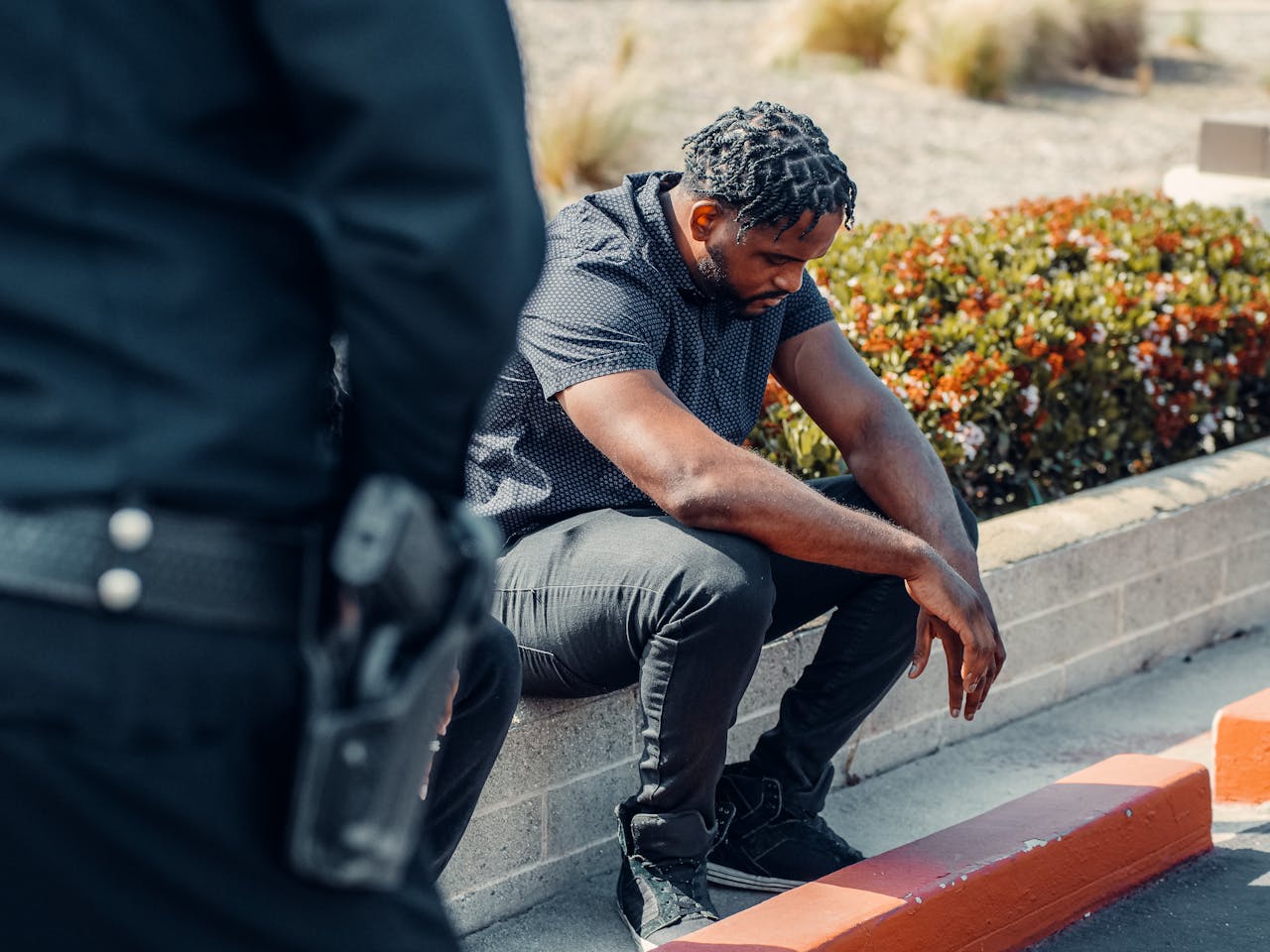 About A police officer watches over a seated suspect outdoors, conveying law enforcement dynamics.
