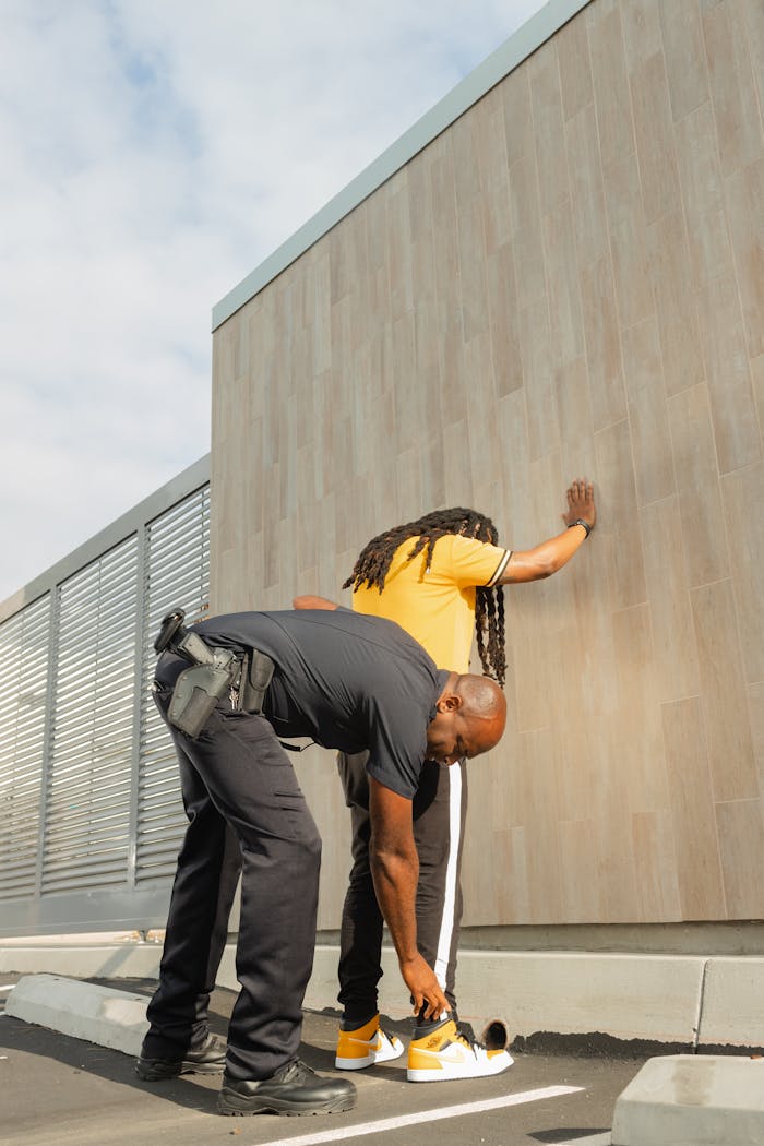 Services A police officer conducts a search on a suspect outdoors against a wall during the day.